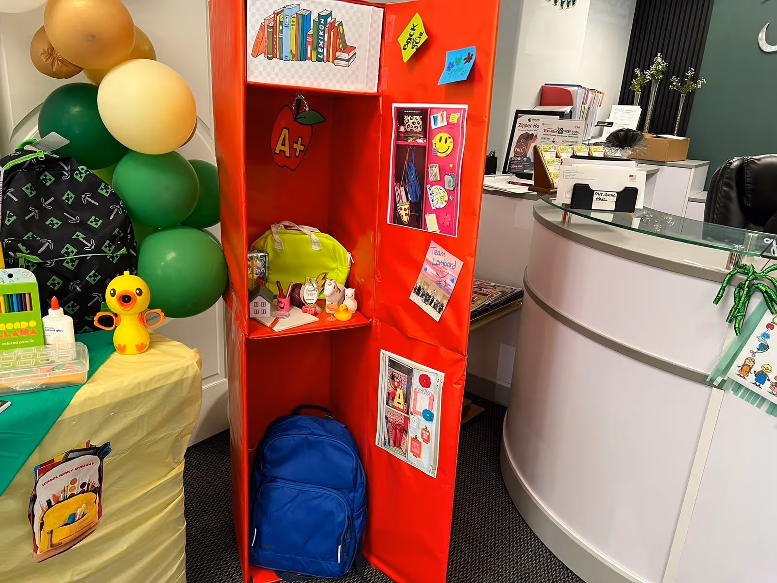 Bright reception area with a red activity display, balloons, toys, and a curved desk.