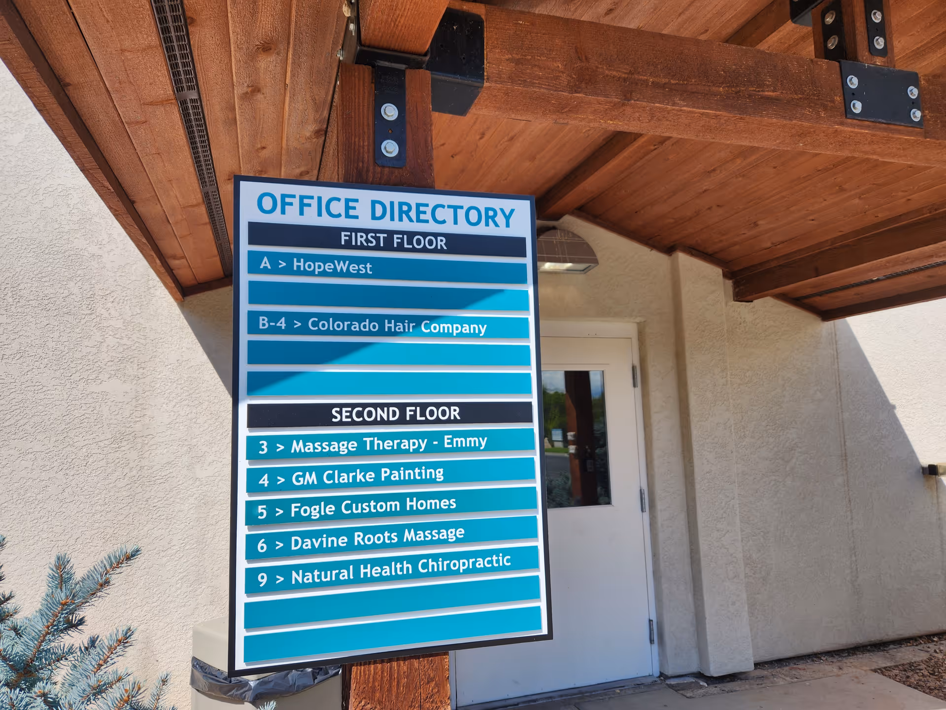 Outdoor building exterior with a blue HopeWest office directory sign beside a white door.