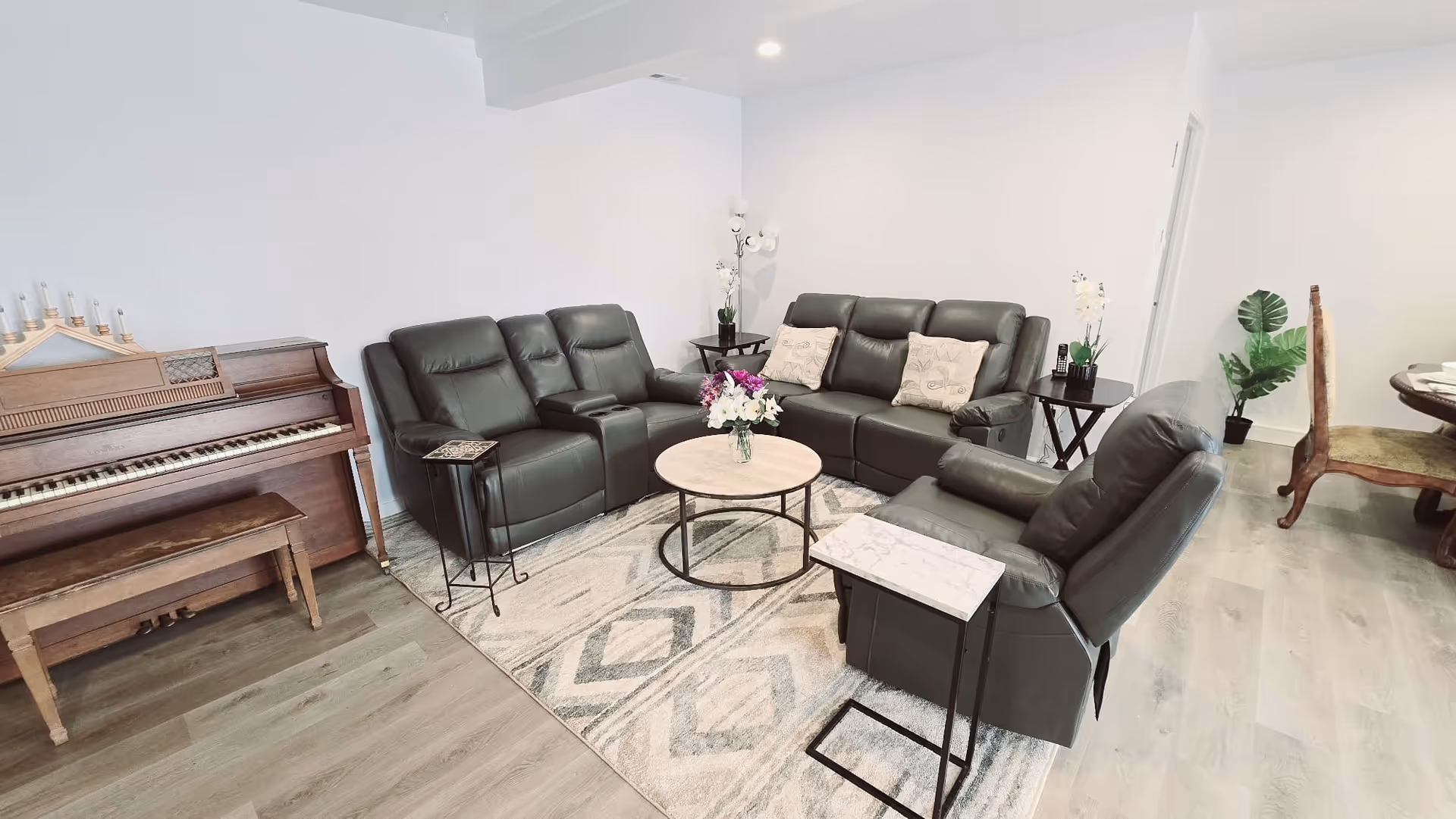 Cozy senior living lounge with black leather seating, piano, coffee table, and plants.
