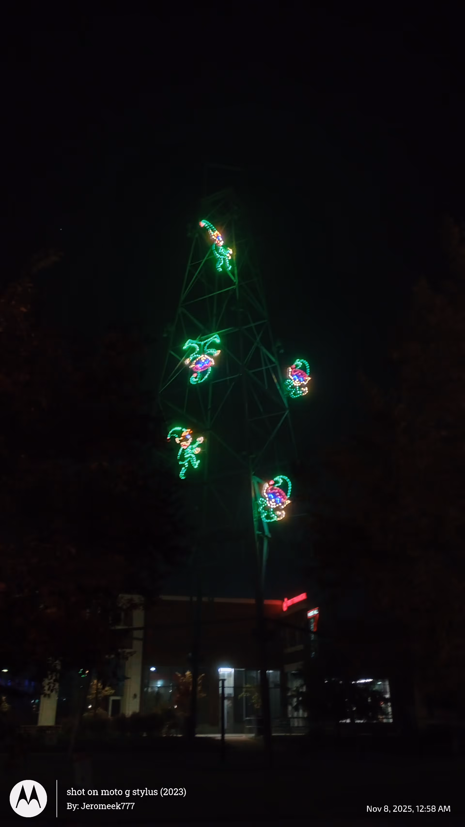 Night exterior of a facility with a tall lattice tower decorated in colorful holiday lights.