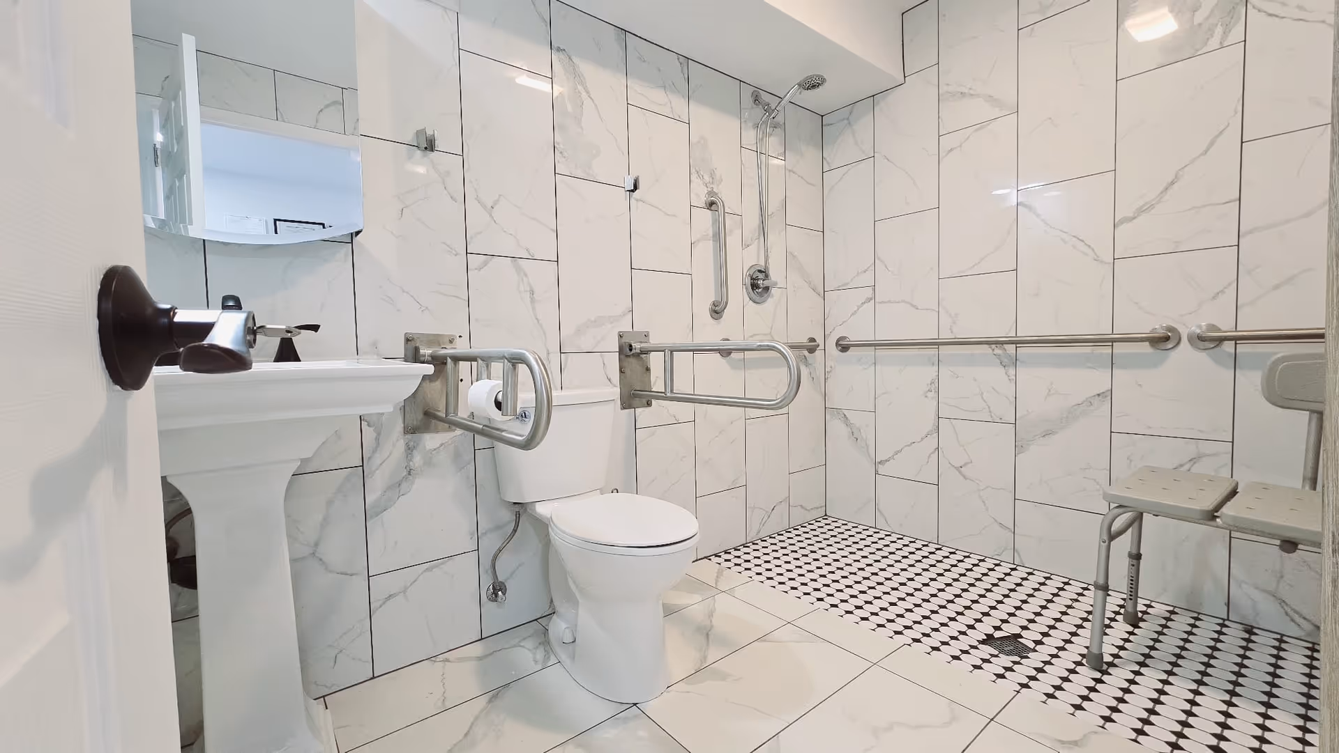 Accessible bathroom with marble walls, toilet, sink, shower, and safety grab bars.