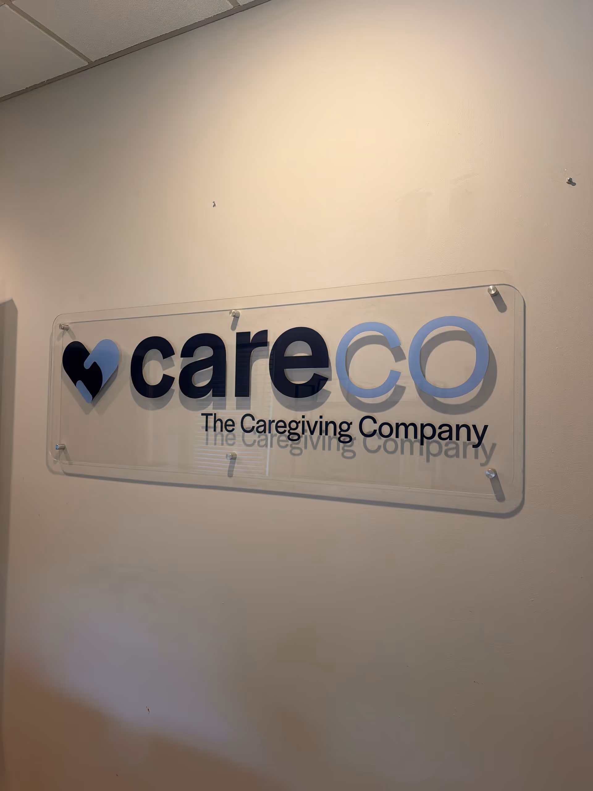 Clear acrylic sign reading careco The Caregiving Company mounted on a wall