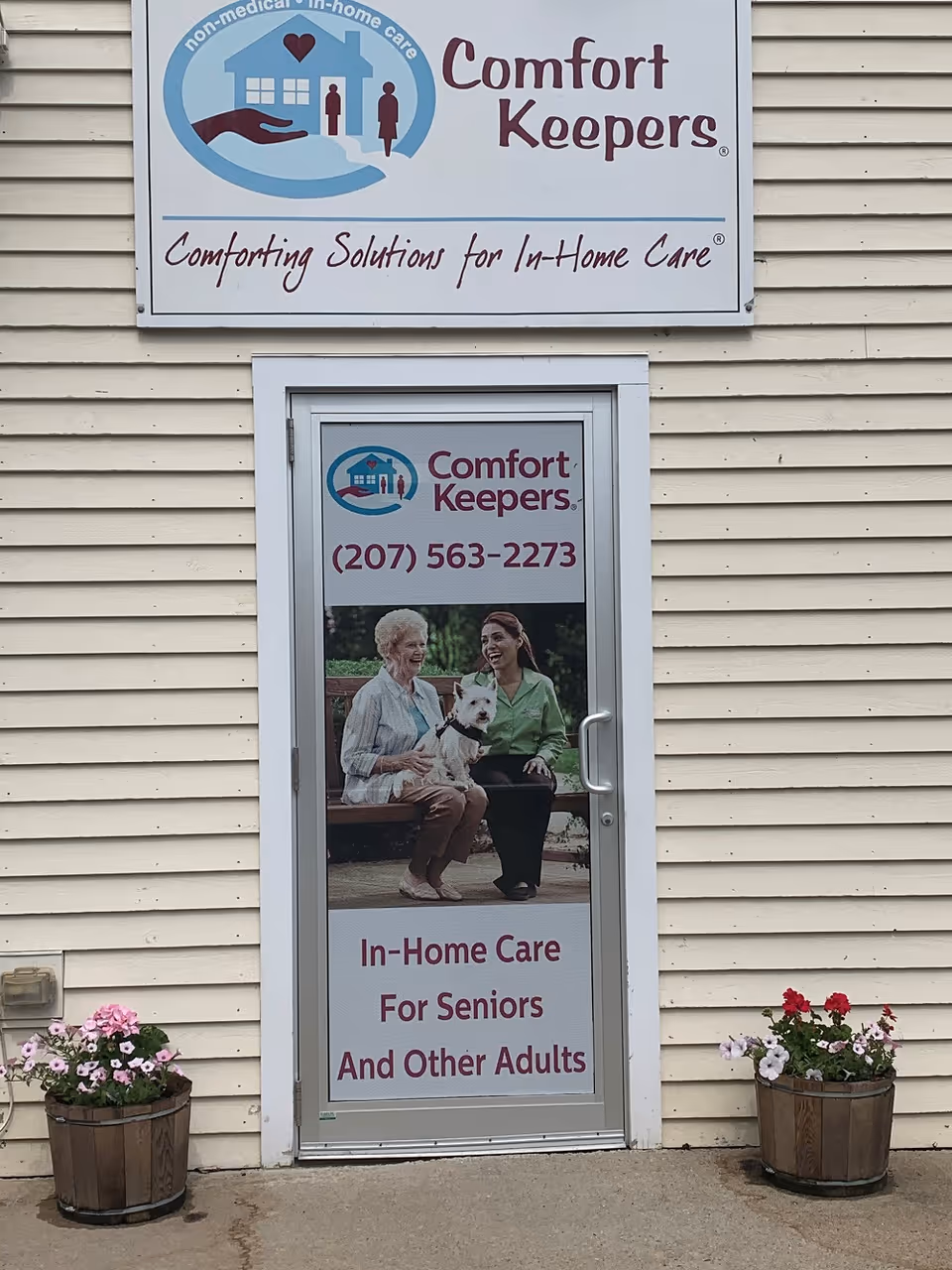 Exterior view of a beige building with Comfort Keepers signage and potted flowers.