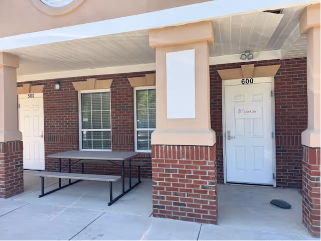 Brick exterior of a building with two doors, a covered porch, and a bench.