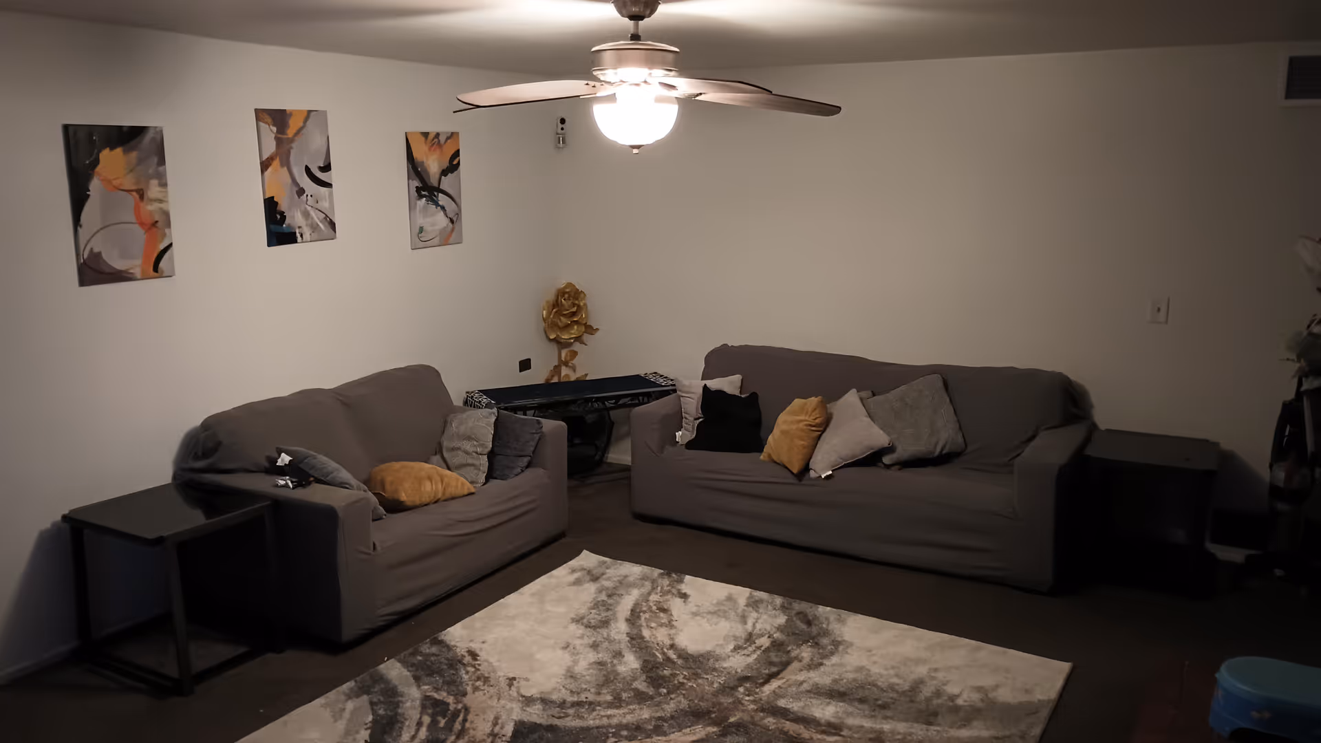 Two gray couches with cushions, a patterned rug, wall art, and a ceiling fan.