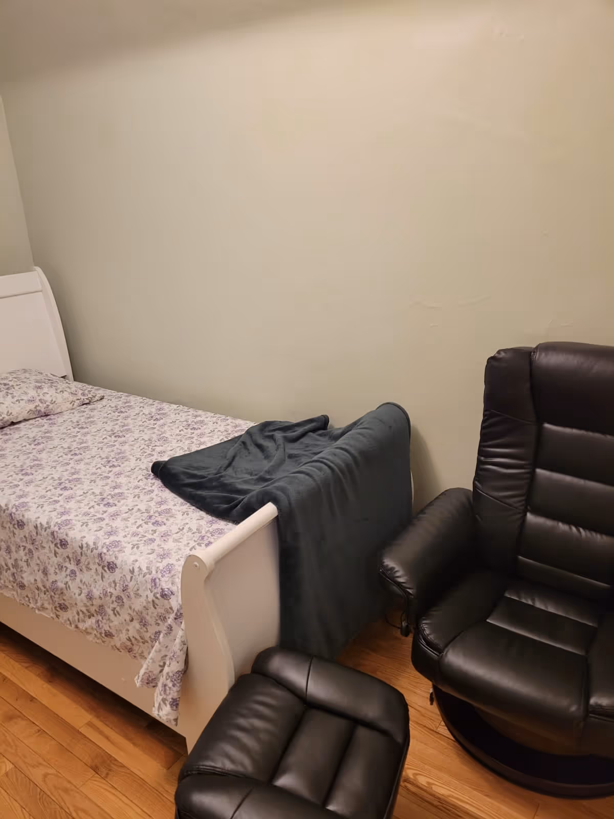 Small bedroom with a floral bed and two black recliners.