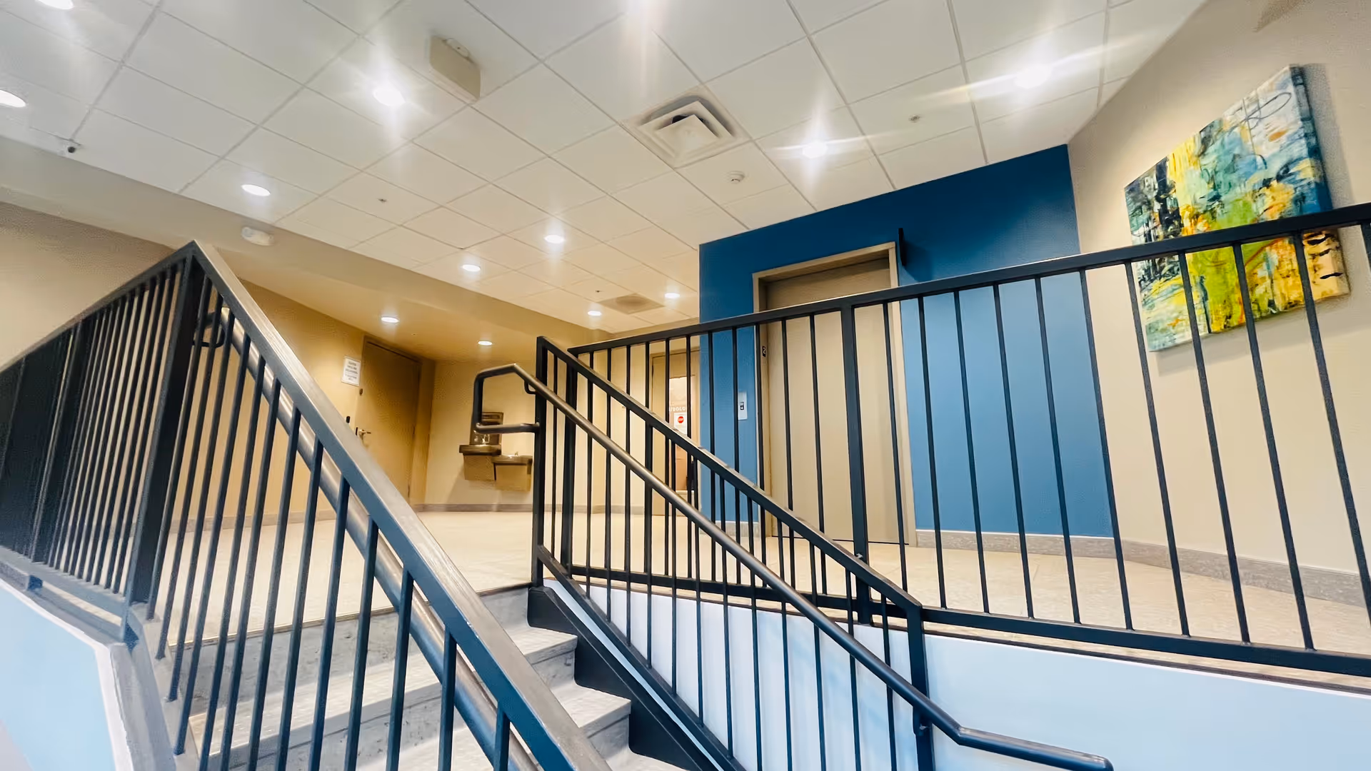 Interior stairwell with metal railing, beige walls, and a blue accent wall in a modern facility.