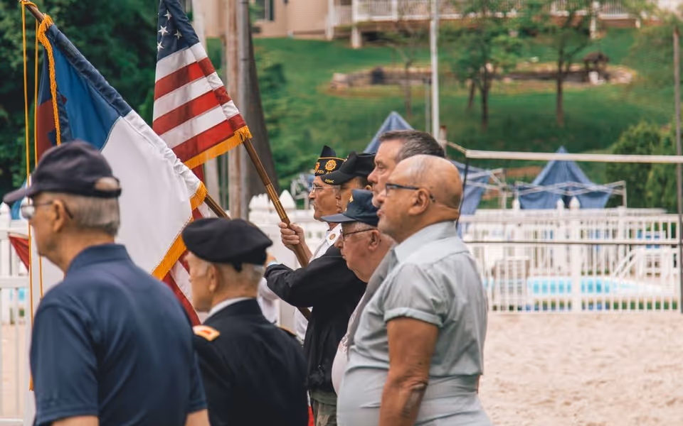Veterans and officials stand in a line with flags at an outdoor ceremony.