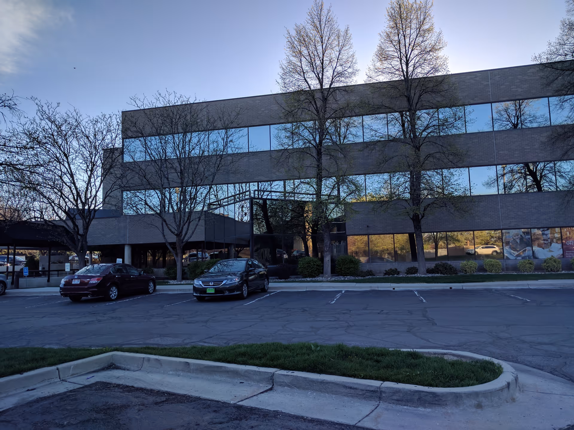 Modern brick office building with glass windows, leafless trees, and parked cars.