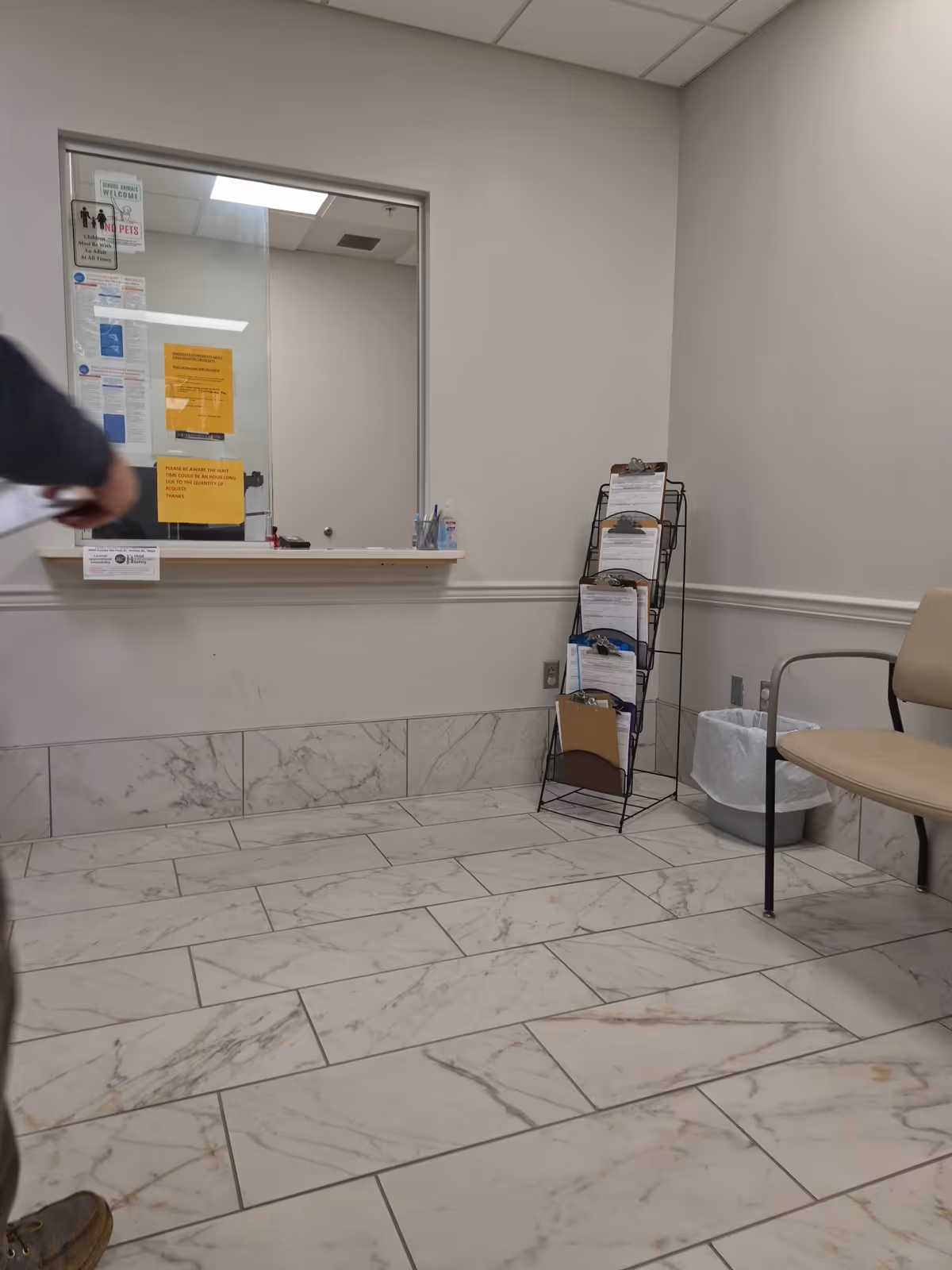 Empty waiting area with marble tiles, brochure rack, and windowed service counter.