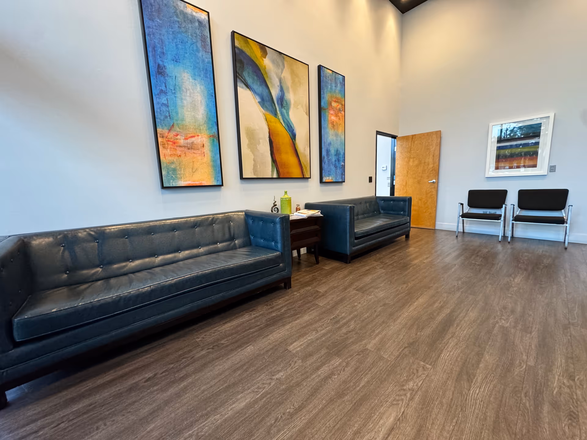 A modern waiting area with blue tufted sofas, artwork, and a wooden floor.