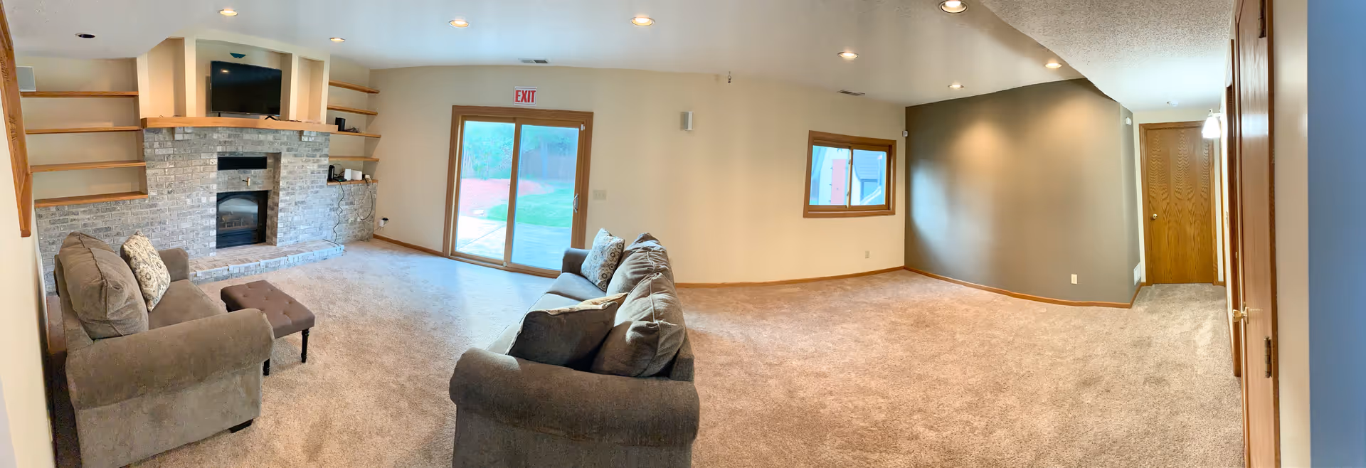 Spacious living area with fireplace, stone wall, sofas, carpet, and exit door.
