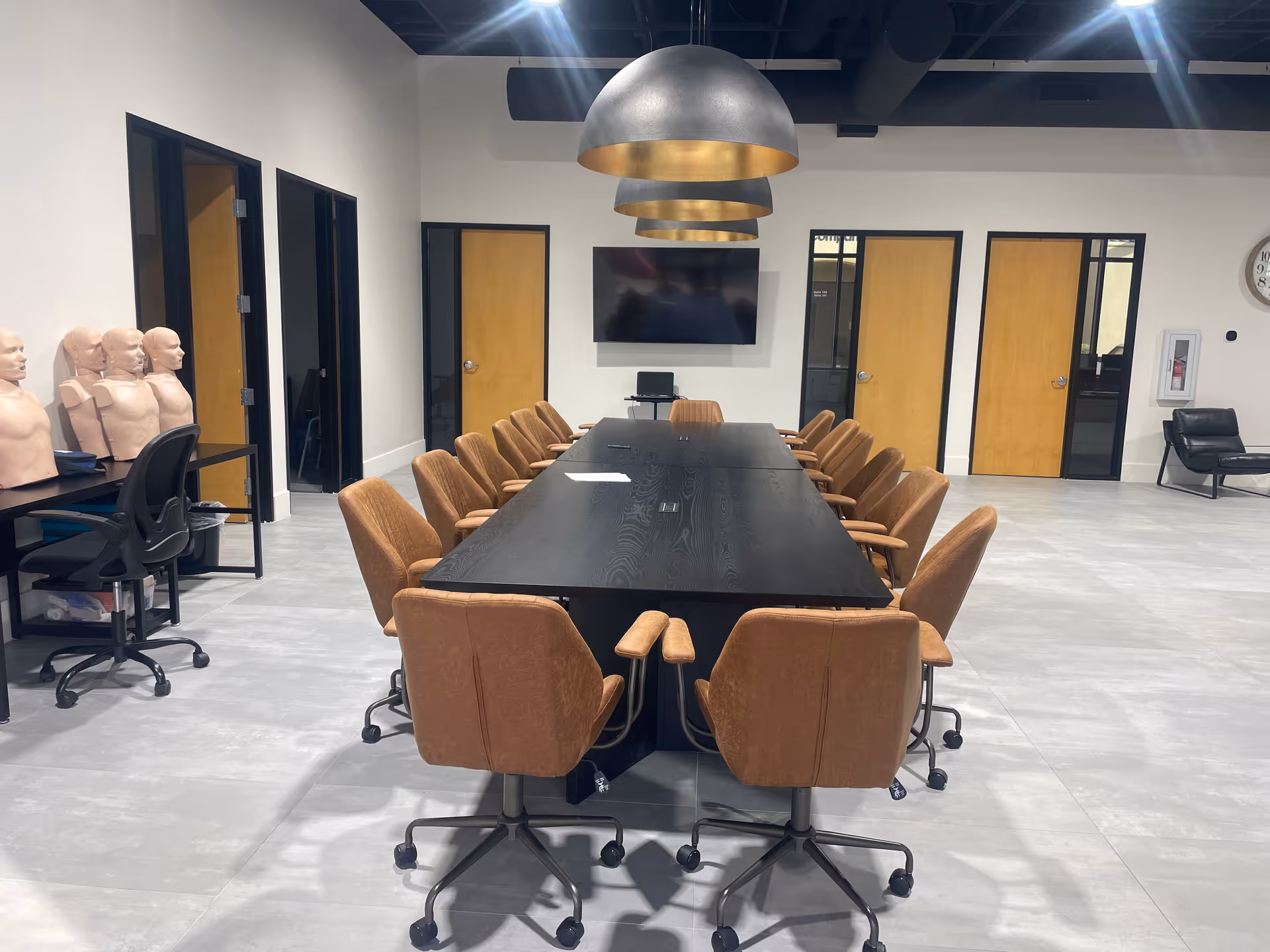 Conference room with a long dark table, brown chairs, TV, and CPR mannequins along left wall.