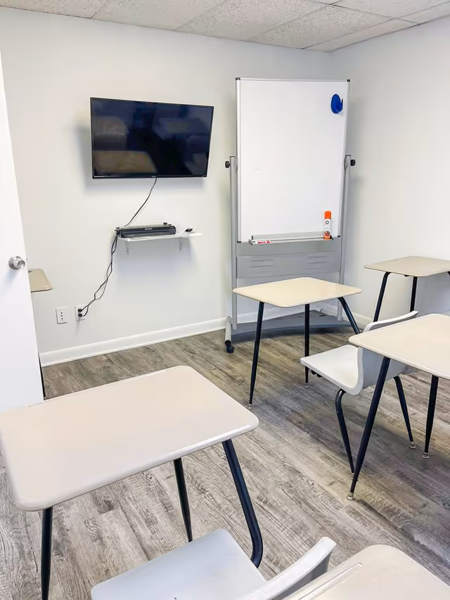 Small classroom-style room with desks, a whiteboard, and a wall-mounted TV.