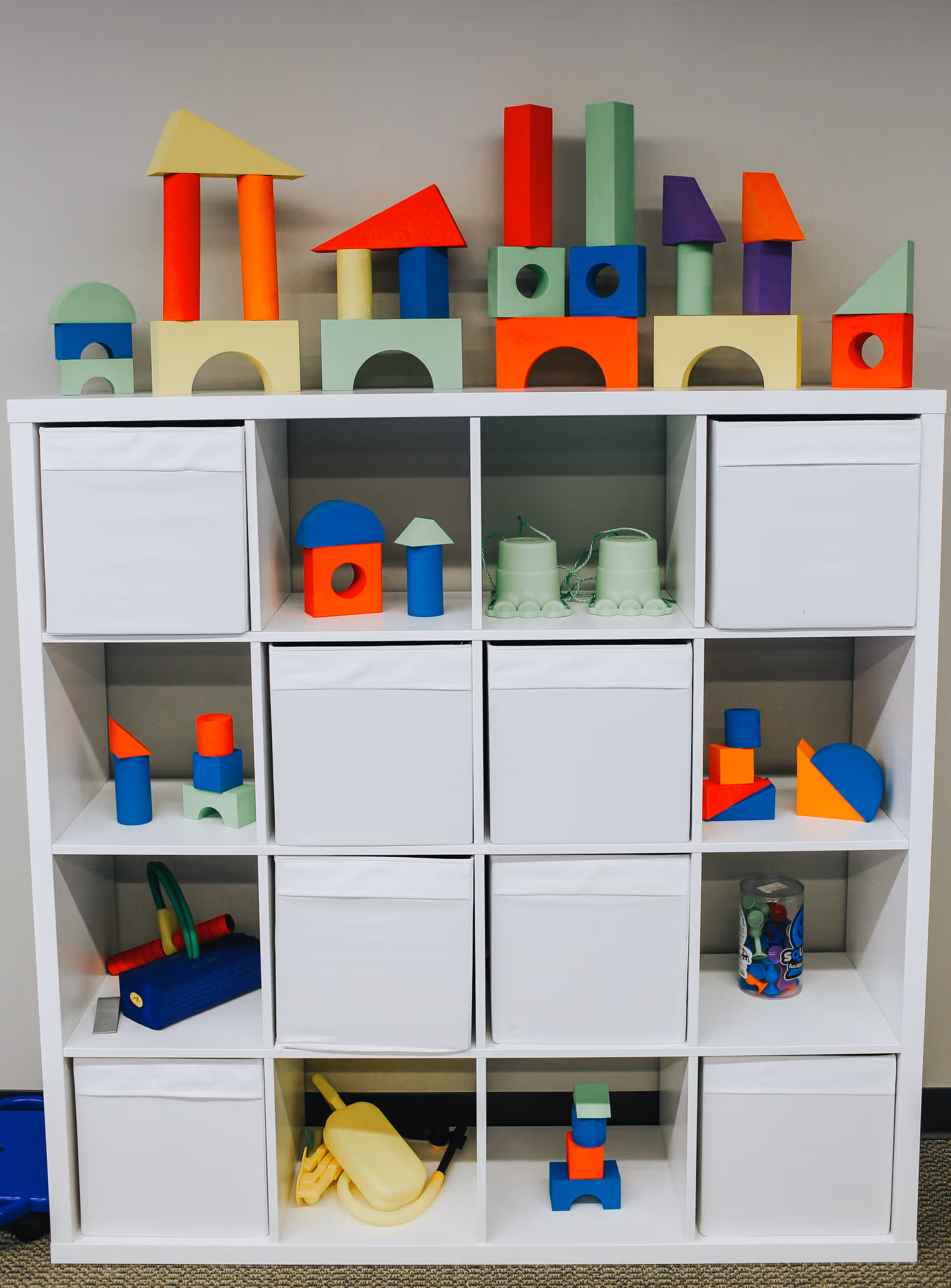 White cubby storage unit topped with colorful wooden blocks and toys.