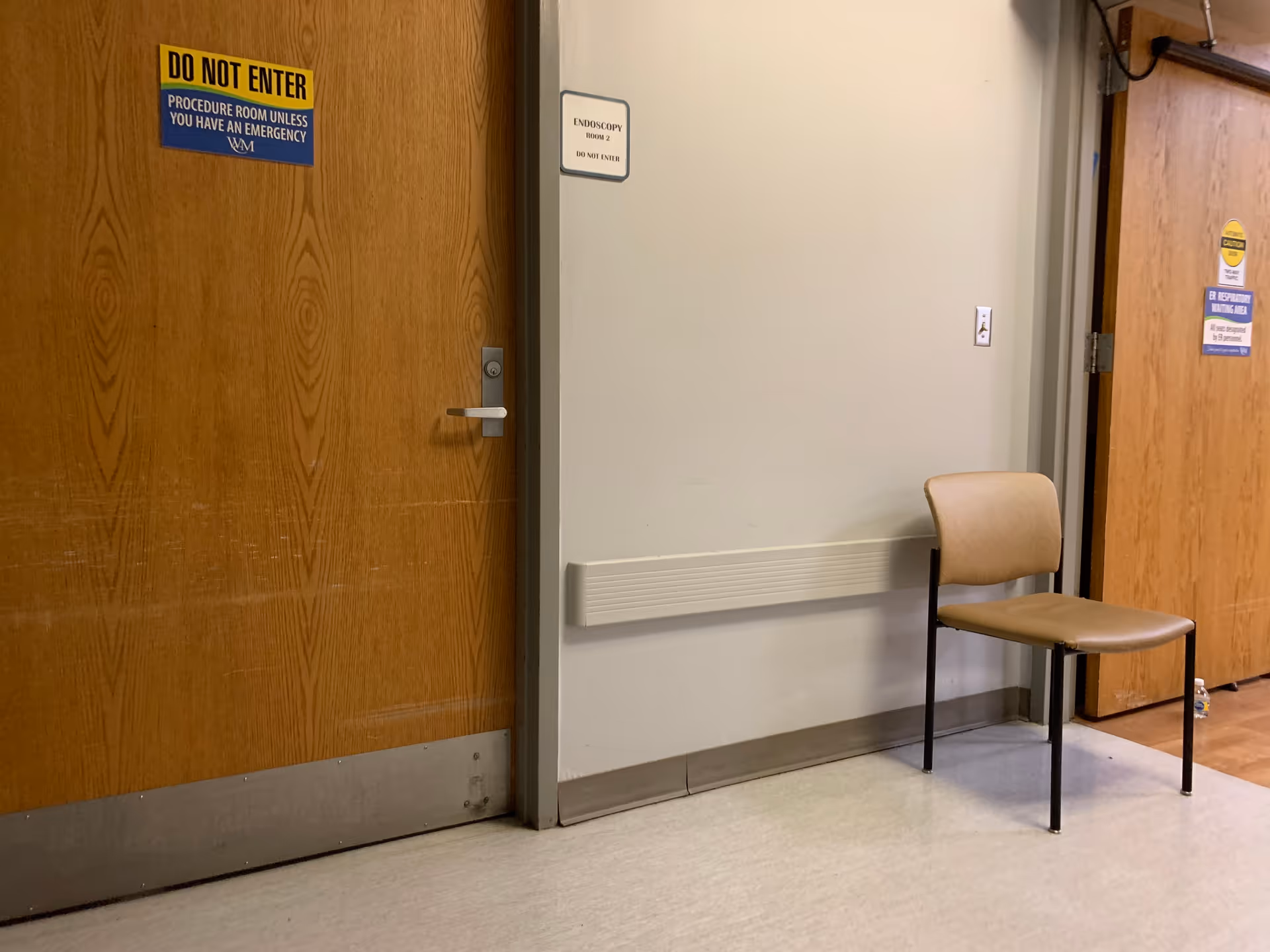 Interior corridor of Weirton Medical Center with wooden doors, a beige chair, and safety signs.