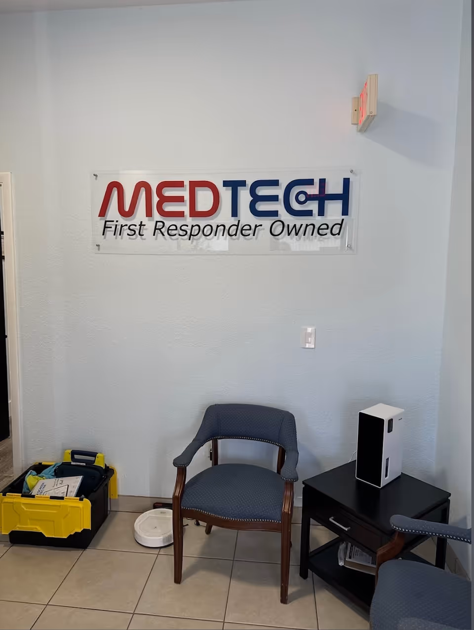 Interior lobby corner with MEDTECH First Responder Owned sign, blue chair, and medical equipment.