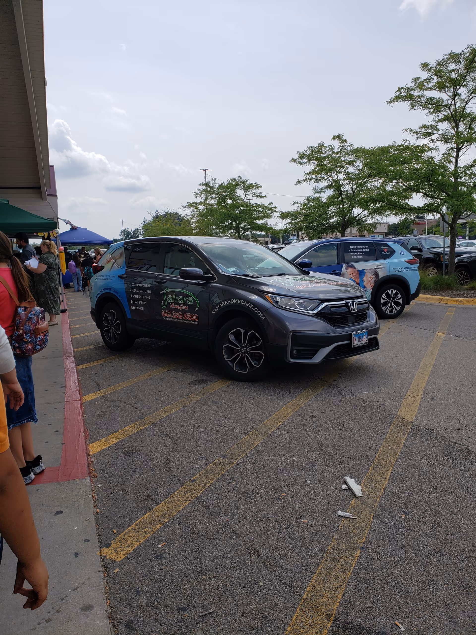 A parking lot outside Sahara Home Care with branded vehicles and people near the entrance.