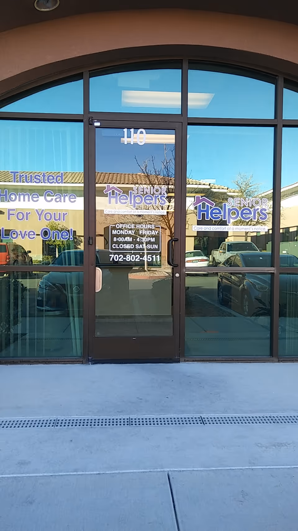 Glass entrance doors show Senior Helpers signage with reflections of parked cars outside