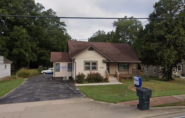 Front view of a small Senior Helpers facility with driveway and signage.