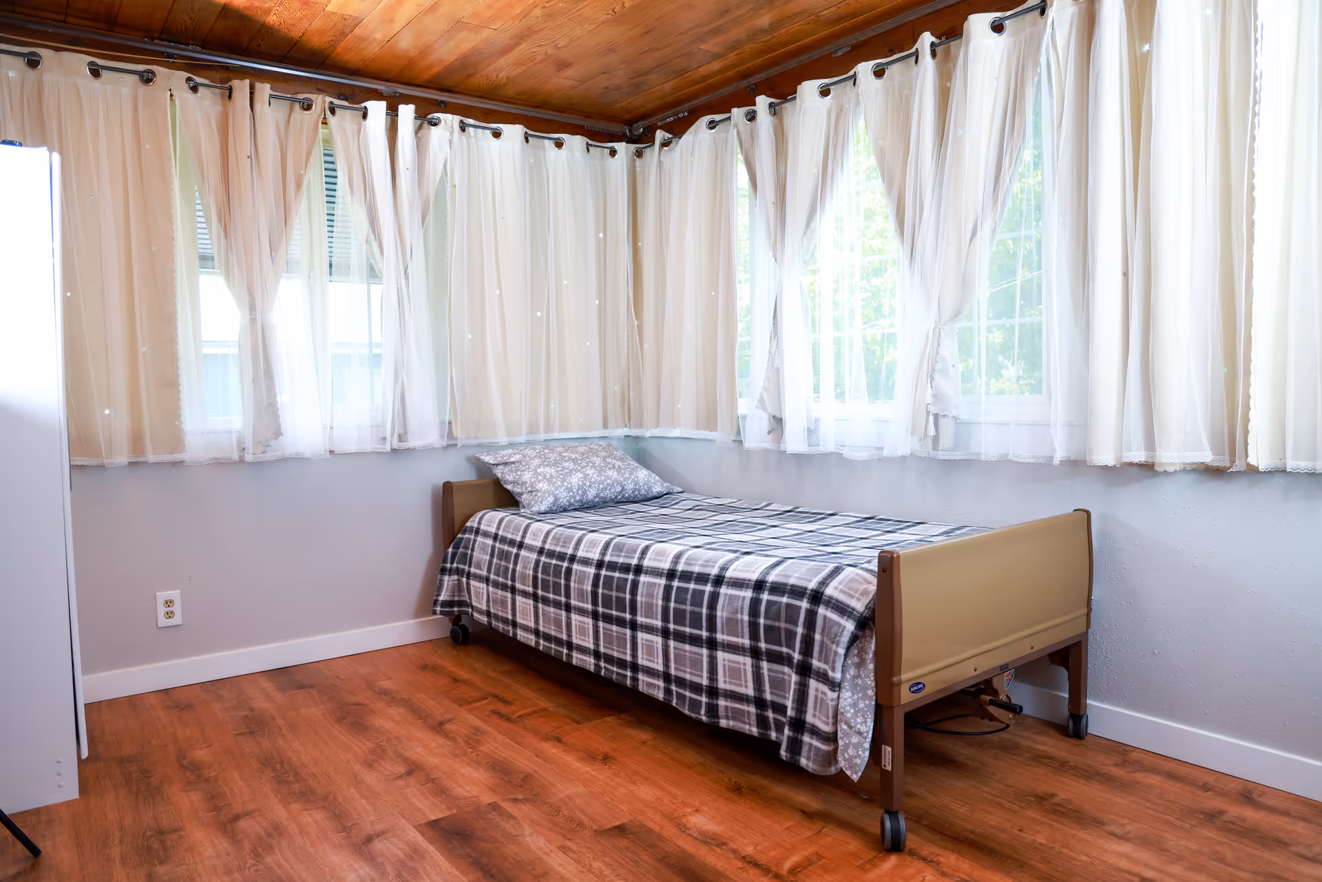 A single bed in a small bedroom with sheer curtains along windows.