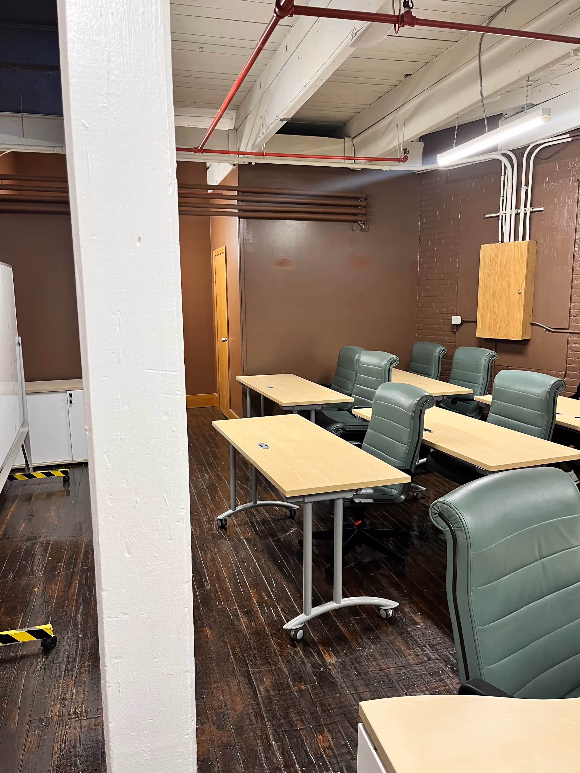 Industrial-style classroom with light wood desks and green chairs arranged in rows.