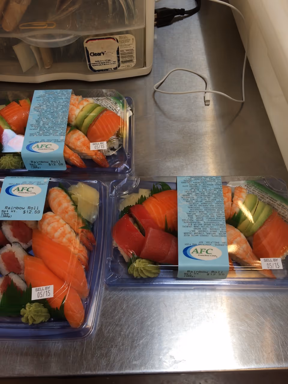 Assorted sushi packs on a stainless steel kitchen counter near a plastic organizer.