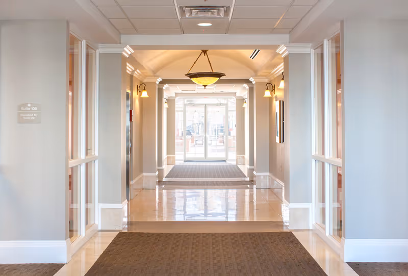 Bright interior hallway with arches, blue-gray walls, and glass doors at the end.
