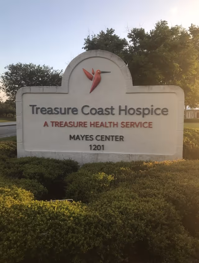 A stone exterior sign for Treasure Coast Hospice Mayes Center sits outside.