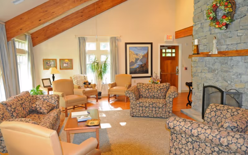 Cozy living room with floral upholstery, a stone fireplace, and bright windows.