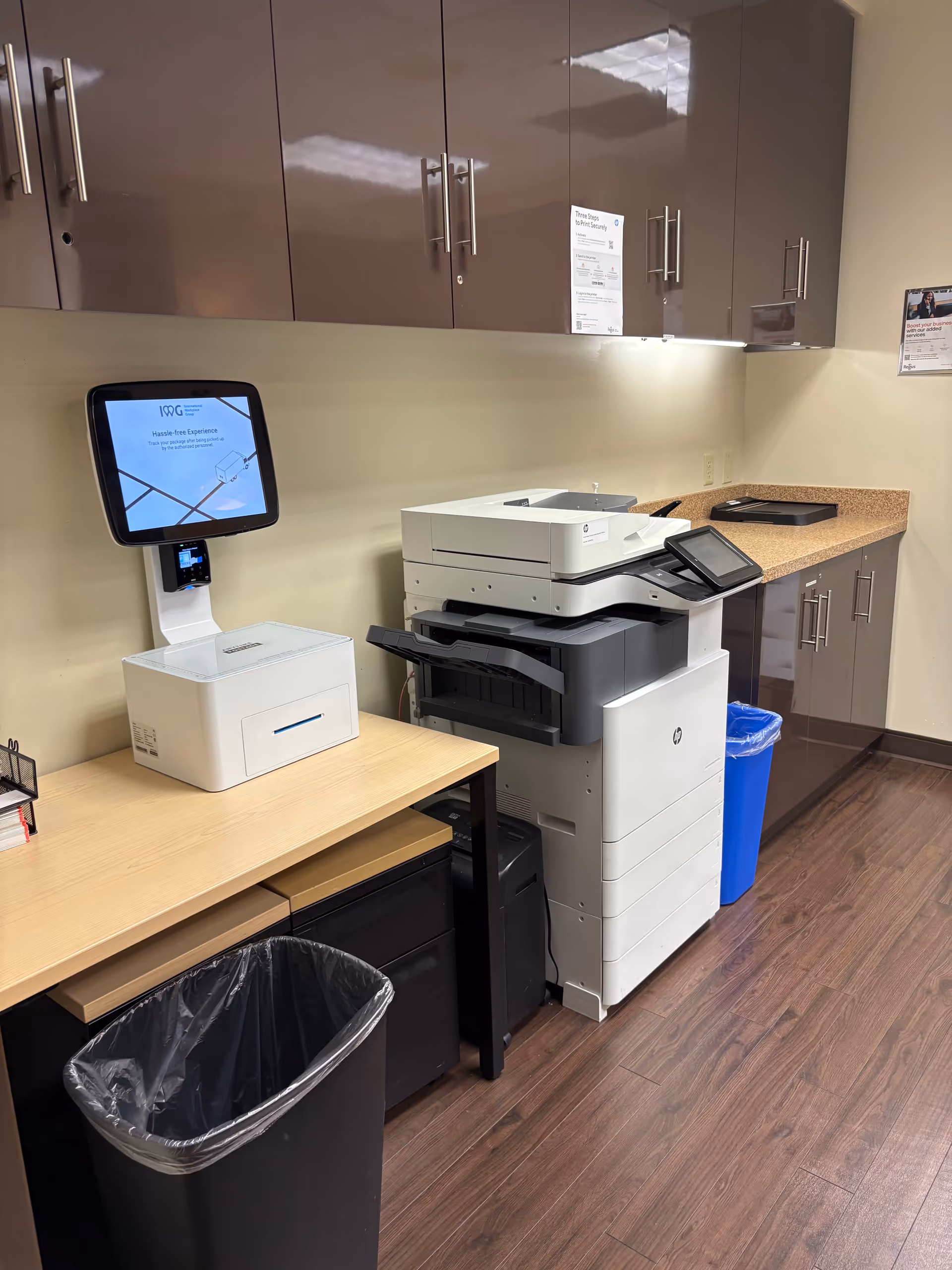Office area with a copier and printer on a desk beneath brown cabinets.