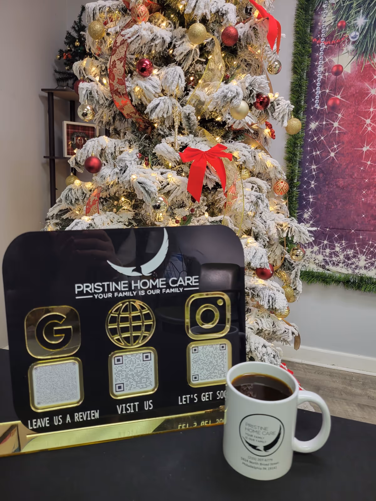 Decorated snow-covered Christmas tree beside a promotional sign and coffee mug indoors.