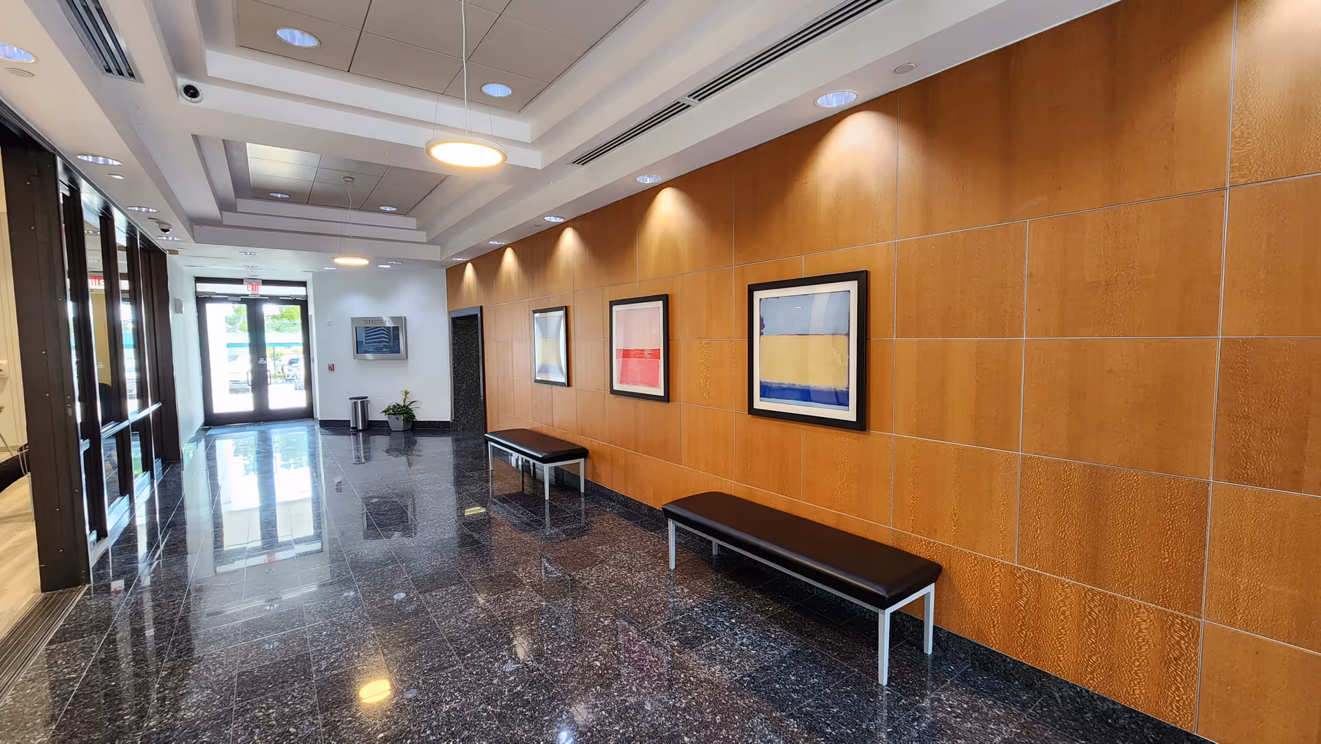 Interior hallway in a senior facility with wood-paneled wall, benches, and framed art.