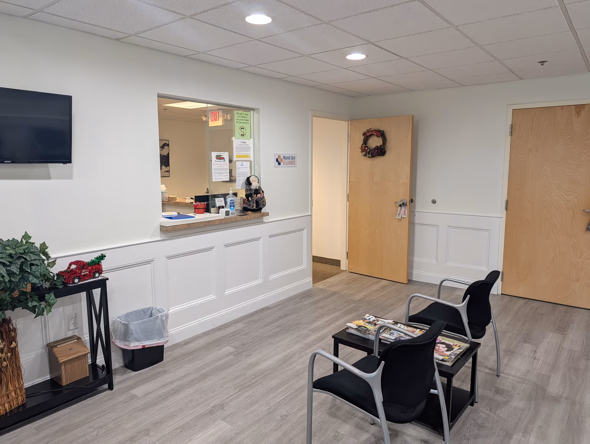 Interior reception area with windowed counter, seating, magazines, and closed doors.