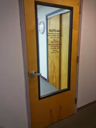 Wooden interior door with a window pane and suite info in a hallway.