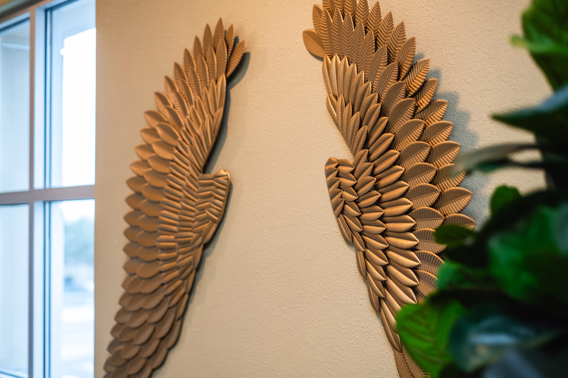 Beige wall with two large metal leaf sculptures beside a window.