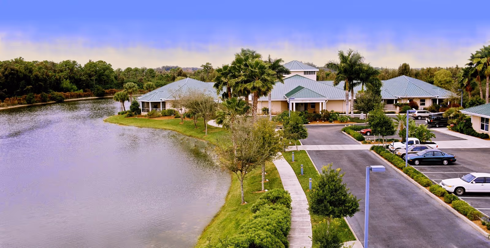 Aerial view of Hope Hospice senior living campus with a lake, palm trees, and parking.