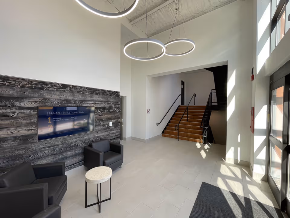 Bright modern lobby interior with circular ring lights, wood panel accent wall, and a stairway.