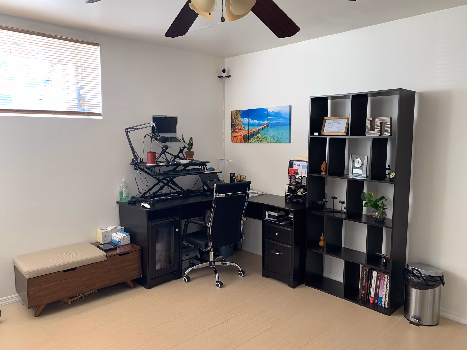 Office corner in a clinic with desk, monitor, shelving, and a window.