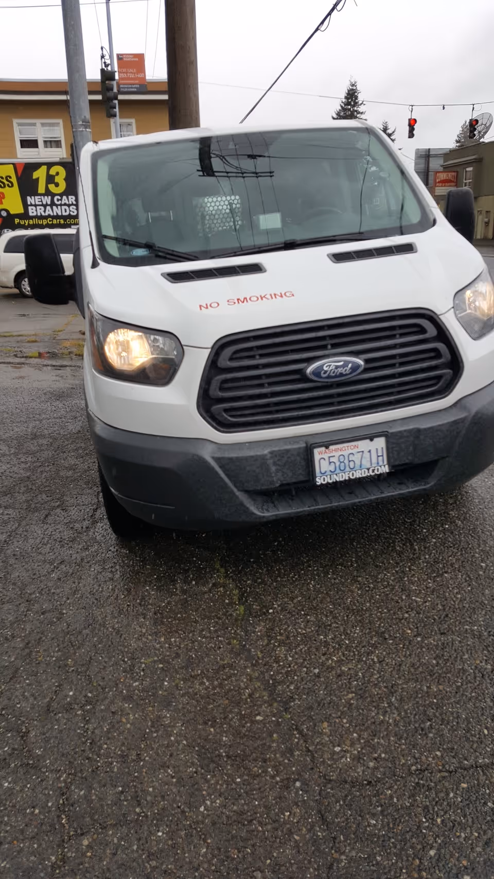 White Ford van with No Smoking on the hood parked on a wet street.