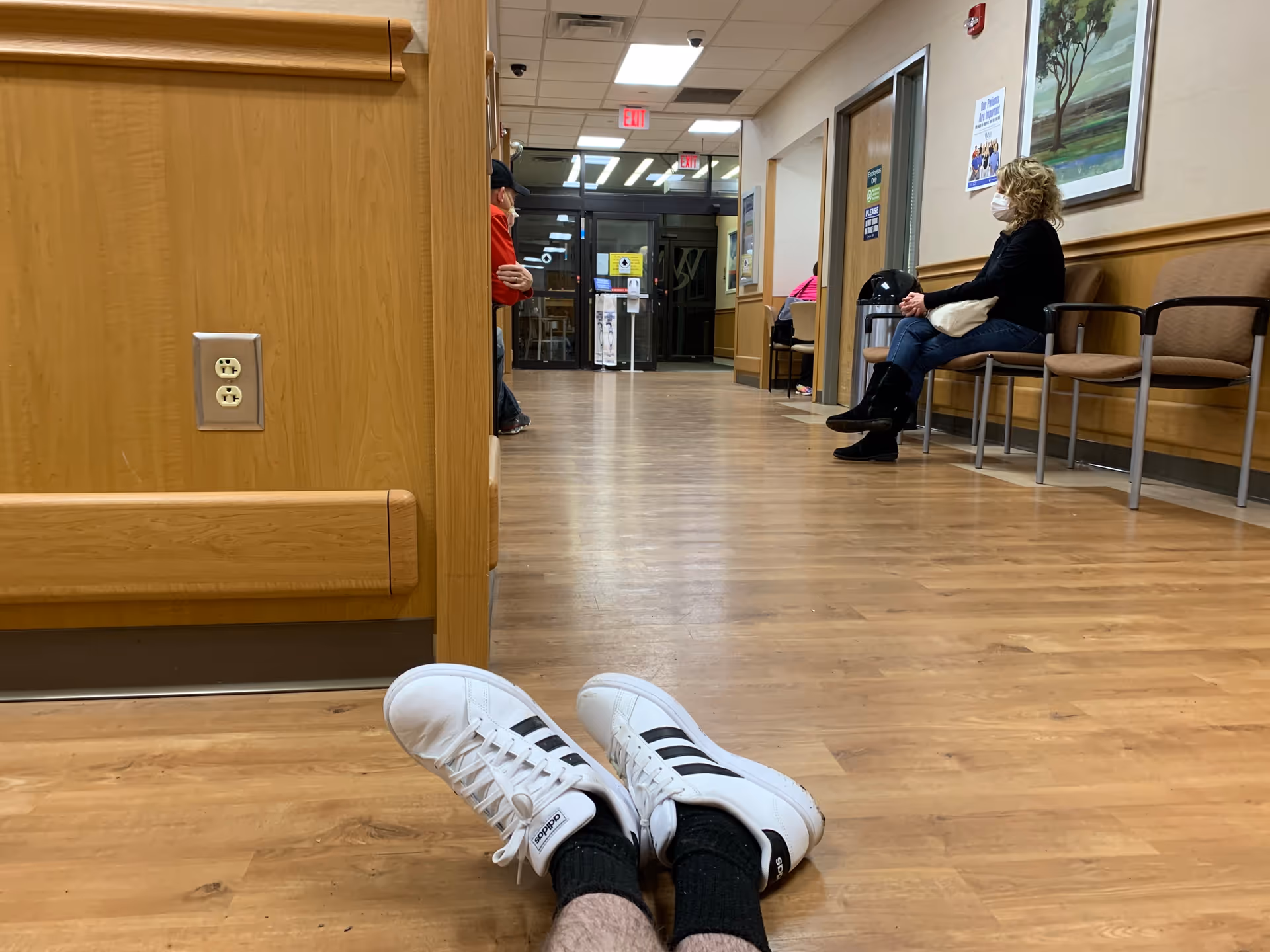 Hospital hallway interior with seated people and feet visible in foreground.