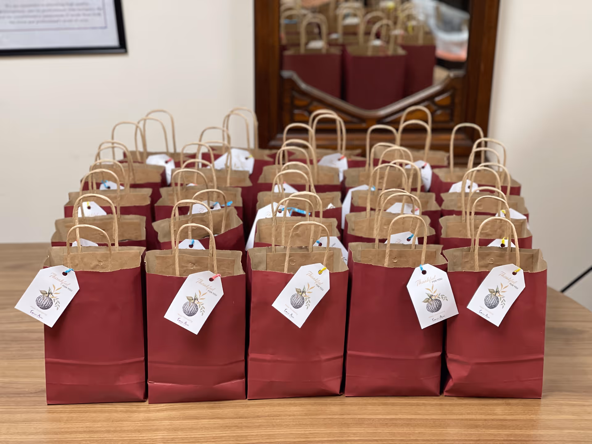 Row of burgundy gift bags with handles arranged on a wooden table indoors.