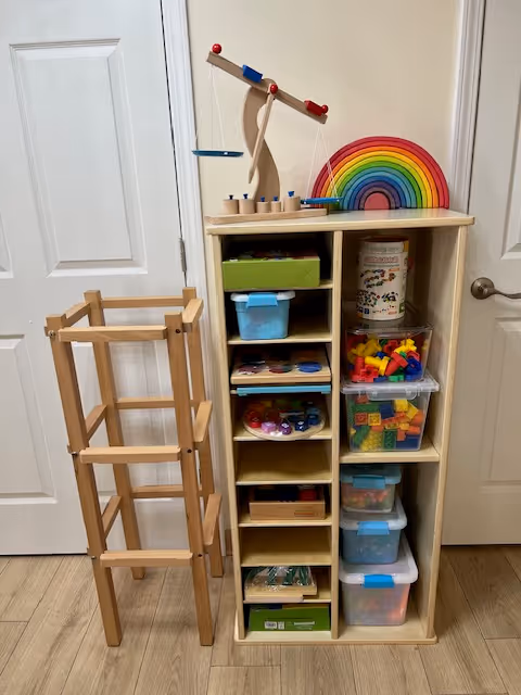 Wooden shelving unit with bins and a rainbow arch toy in a bright interior.