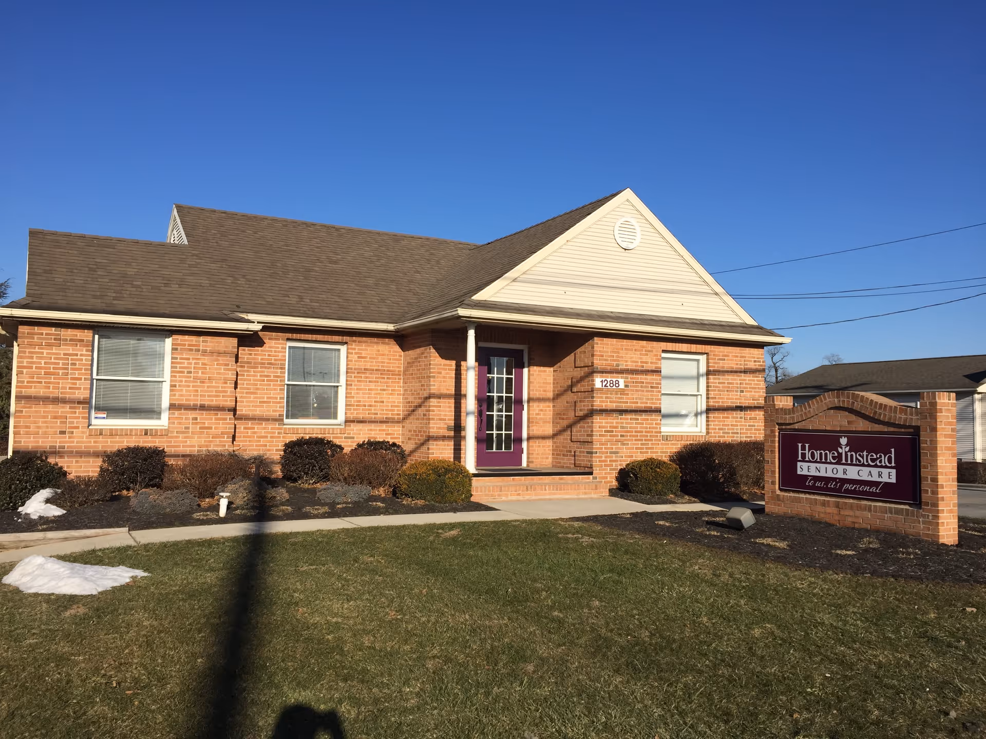 Exterior view of a brick Home Instead building with a purple front door and sign.