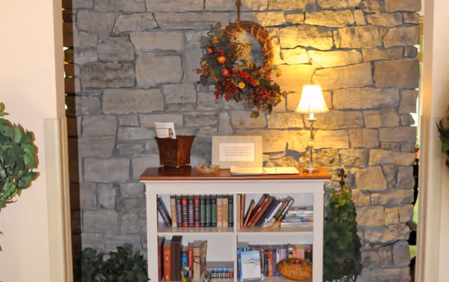 Stone accent wall with wreath, lamp, and bookshelf in a hospice lobby.