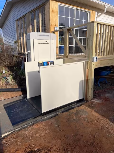 Outdoor platform lift beside a deck, attached to a house with large windowed doors.
