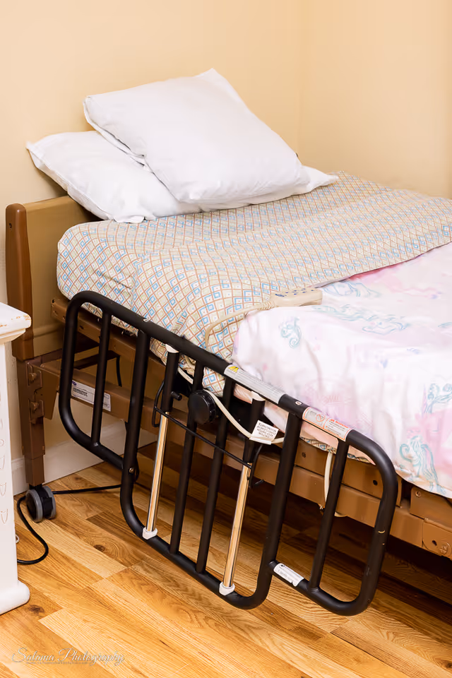 Hospital-style adjustable bed with rails and pillows in a softly colored bedroom.