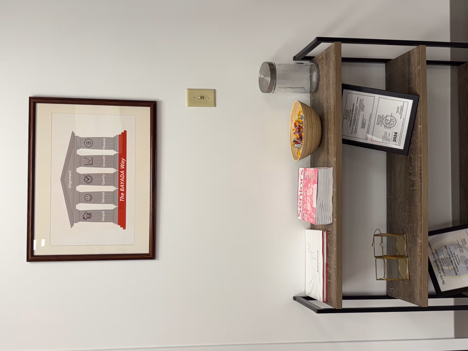 Interior wall with BAYADA poster and wooden shelf displaying certificate and brochures.