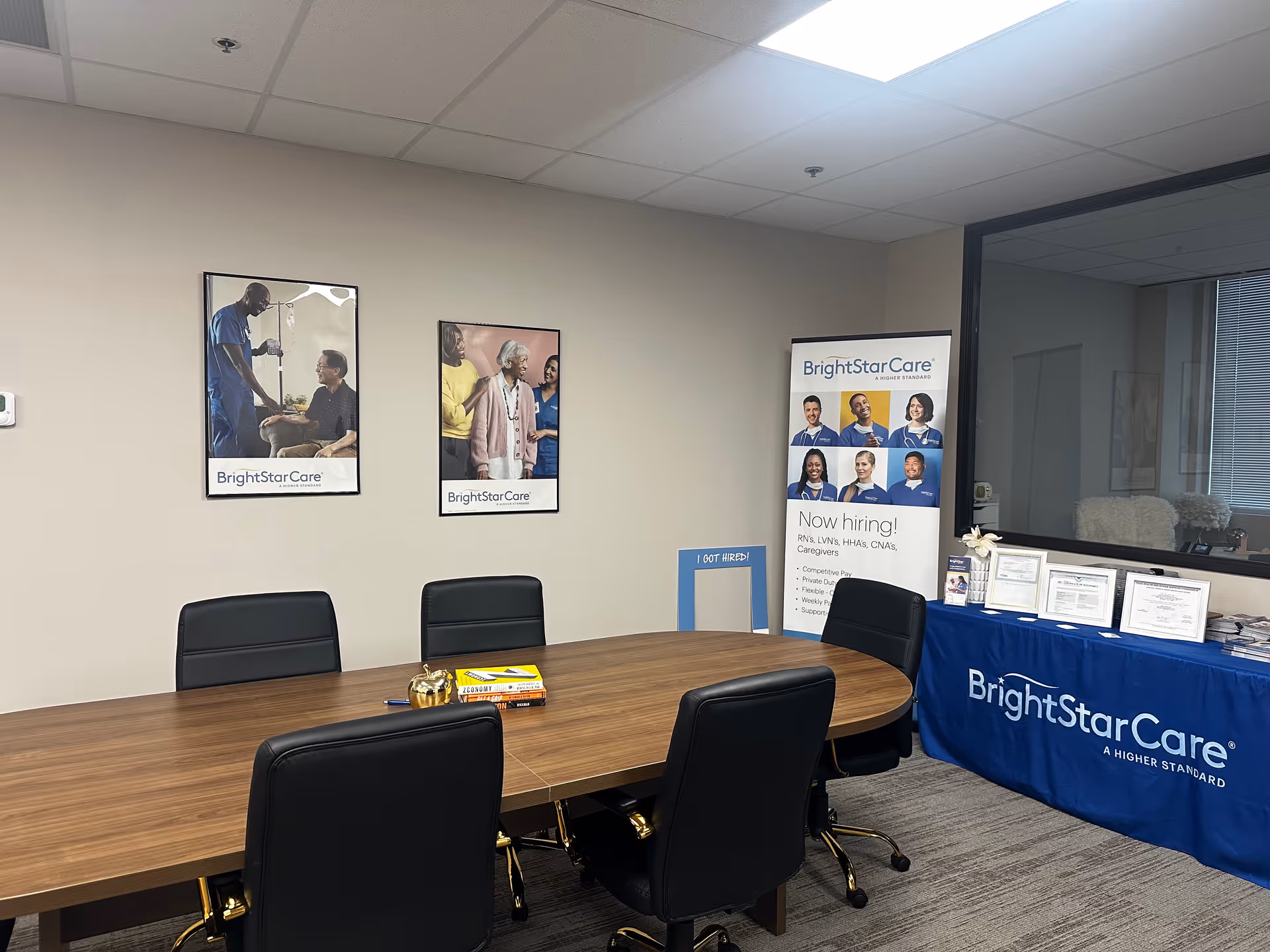 Conference room with a long wooden table, black chairs, posters, and BrightStar Care banner.