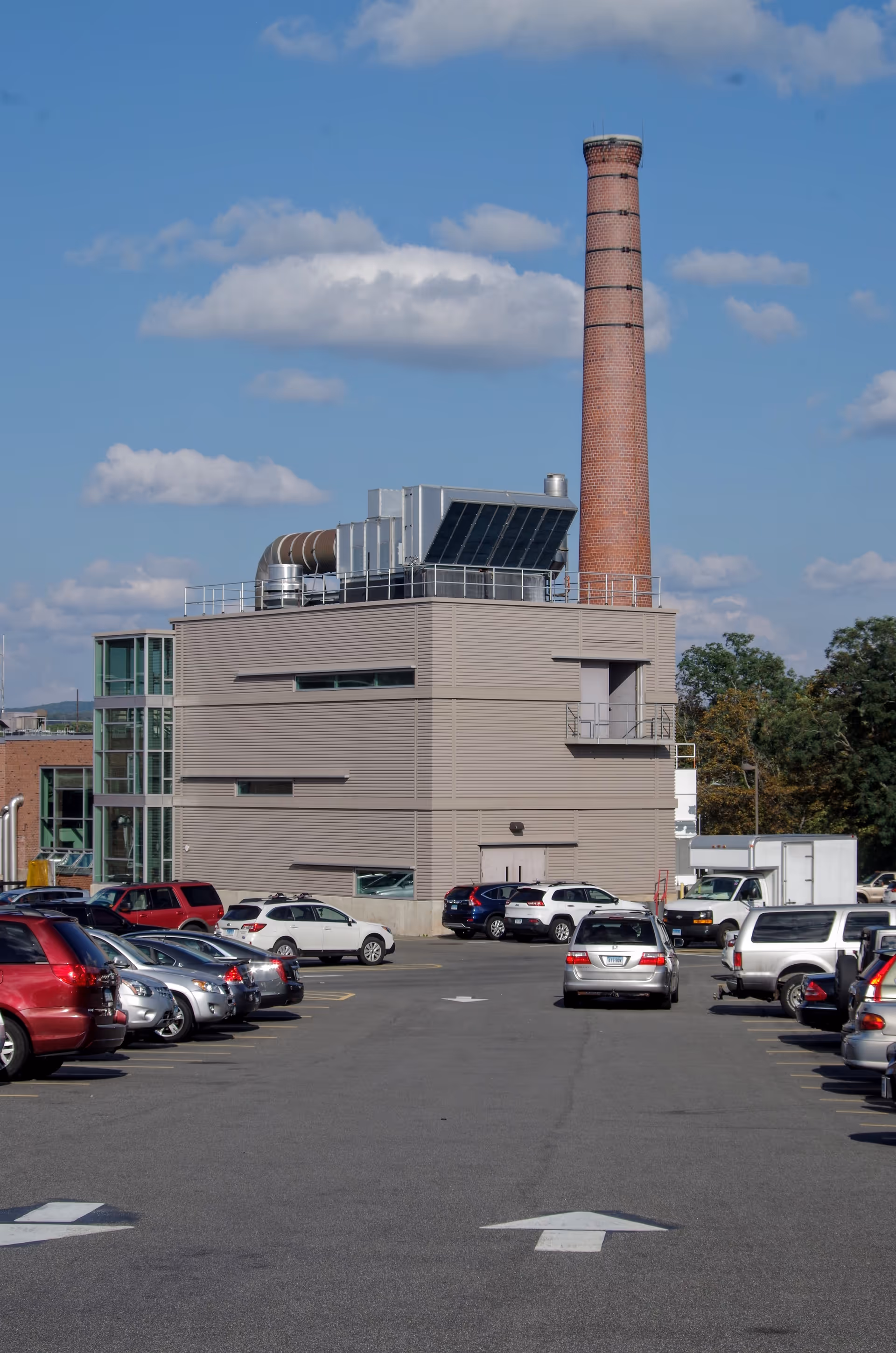 Exterior view of a modern hospital building with a tall brick smokestack and parking.
